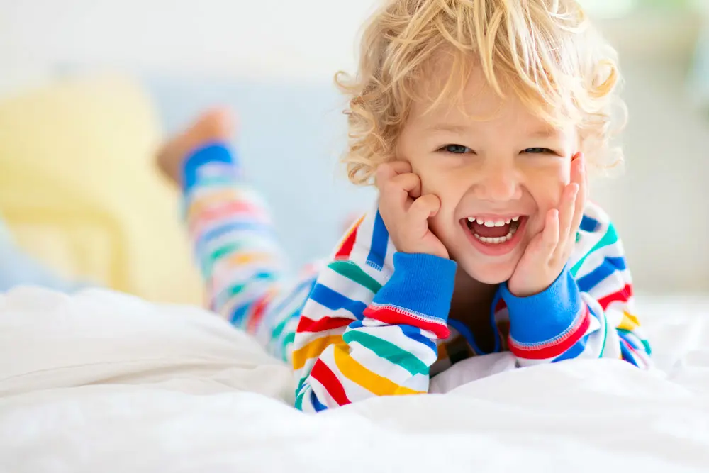 Vediamo in primo piano un bambino sorridente disteso su un letto